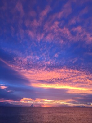 Um pôr do sol sobre o oceano, com céu claro e terra distante.