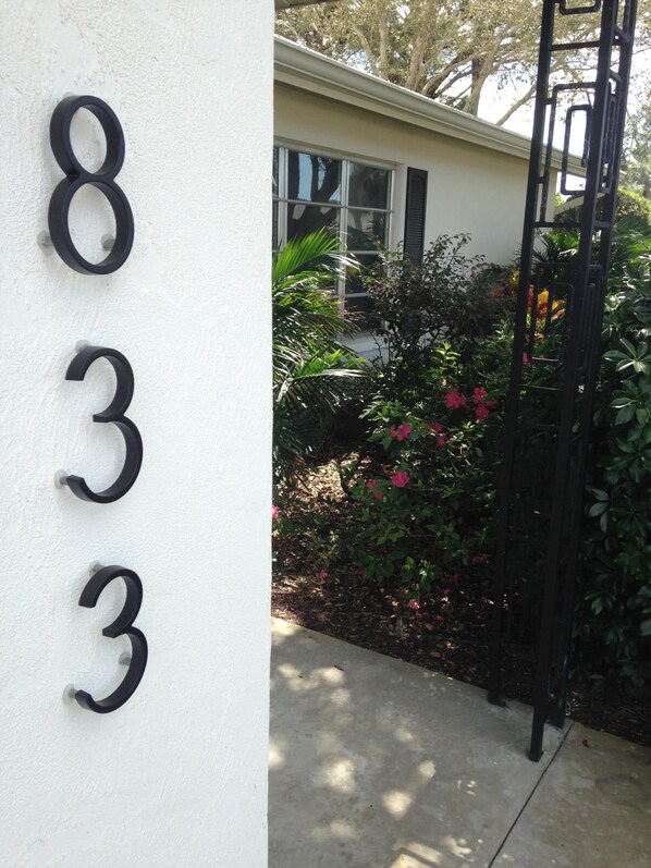Número '833' numa parede branca, com um jardim e um portão de metal preto ao fundo.