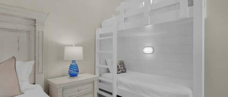 A bunk bed room with a white dresser and a lamp.