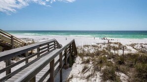 A wooden boardwalk leading to a beach with clear turquoise water and a few people in the distance. - Good Day Sunshine | 100 Steps to Beach | 8 Free Beach Chairs through October! | Huge Private Pool & Lush Backyard (Miramar Beach)