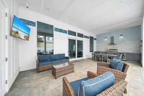 A spacious patio with wicker furniture, a flat-screen TV, and a kitchen area with a grill.
