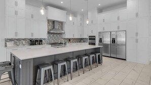 A modern kitchen with white cabinets, a large island with bar stools, stainless steel appliances, and pendant lighting. - Good Day Sunshine | 100 Steps to Beach | 8 Free Beach Chairs through October! | Huge Private Pool & Lush Backyard (Miramar Beach)