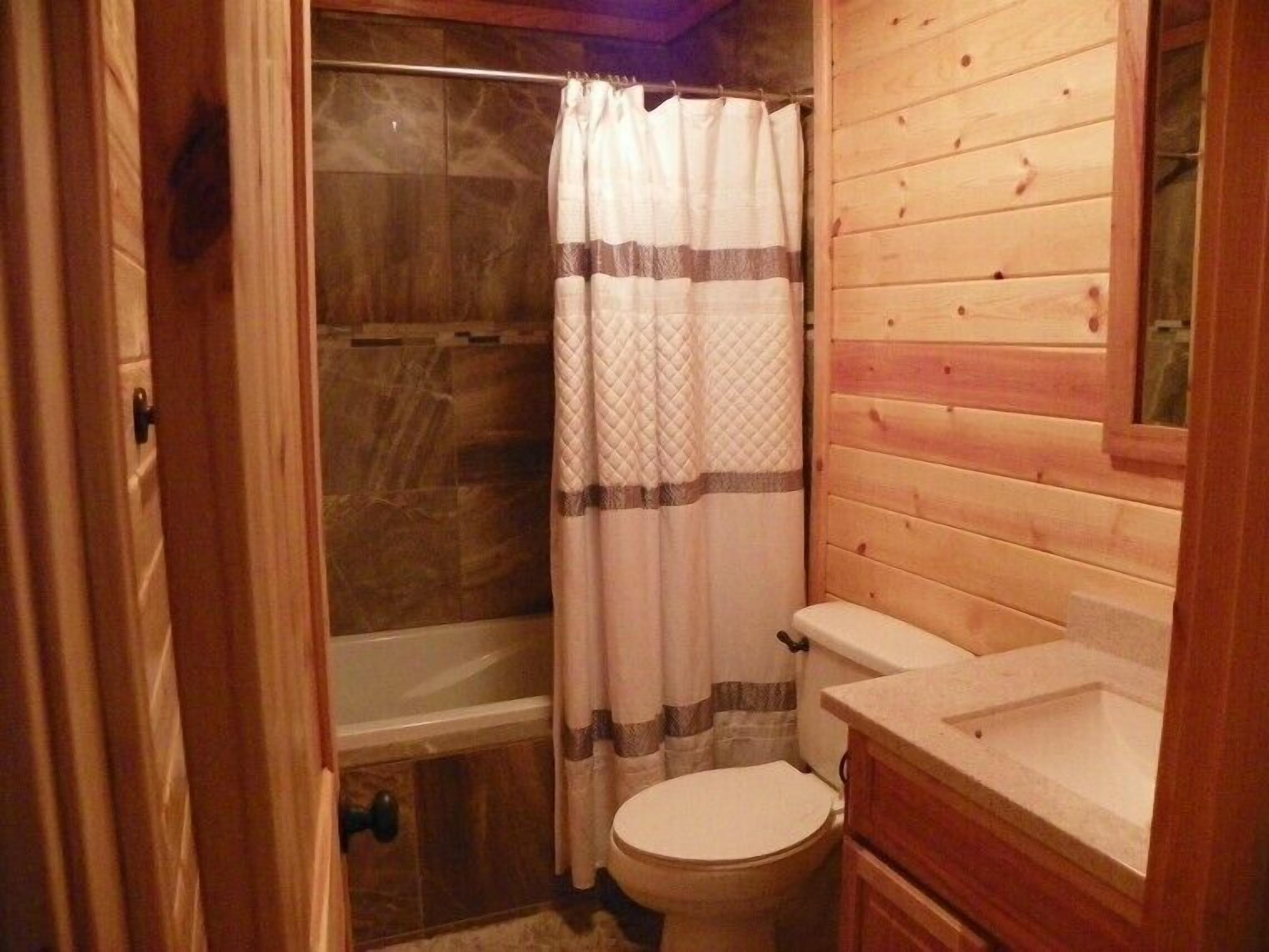 A wooden cabin bathroom with a shower, toilet, and sink.