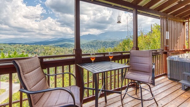Una terraza de madera con dos sillas y una mesa, con vistas a un paisaje montañoso.