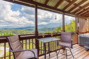 Una terraza de madera con dos sillas y una mesa, con vistas a un paisaje montañoso.