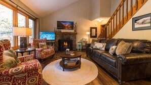 A cozy living room with a fireplace, leather sofa, patterned armchairs, and a television. - Beautifully Furnished, Clean, Cozy Cabin Next to Rocky! Walk to RMNP & YMCA (Estes Park)