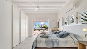 A bedroom with a bed, a nightstand, a lamp, and a view of the beach. - Ocean front Villa on the most magnificient location, only 3 steps from the ocean (Belnem Bonaire)
