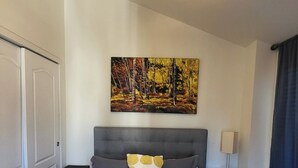 A hotel room with a bed, a ceiling fan, a painting, a nightstand, and a lamp. - Stay at Roosevelt Row / Modern 2BR 2BA Condo (Phoenix)