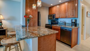 A modern kitchen with granite countertops, wooden cabinets, a built-in microwave, a dishwasher, and a coffee maker. - Romantic Oceanfront Condo at Lahaina Shores with Sweeping Ocean Views (Lahaina)