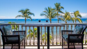 A balcony with wicker chairs and a table, overlooking a beach with palm trees and the ocean. - Romantic Oceanfront Condo at Lahaina Shores with Sweeping Ocean Views (Lahaina)