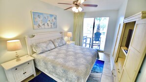 A bedroom with a bed, nightstands, a ceiling fan, a painting, and a view of the outdoors. - Destin West Gulfside #214 ~Free Beach Service! ~Multiple Pools & Lazy River! (Fort Walton Beach)