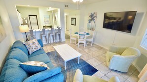 A living room with a sofa, armchairs, a coffee table, and a TV. There is a dining area with chairs and a table. - Destin West Gulfside #214 ~Free Beach Service! ~Multiple Pools & Lazy River! (Fort Walton Beach)