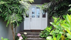 A front entrance with a white door, stone steps, and lush greenery. - Ocean View Retreat in Carmel Meadows w/ Hot Tub. Walk to Trails & Beach! (Carmel)