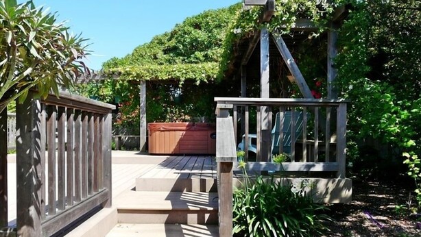 A wooden deck with steps leading to a covered area, surrounded by lush greenery and a hot tub. - Ocean View Retreat in Carmel Meadows w/ Hot Tub. Walk to Trails & Beach! (Carmel)