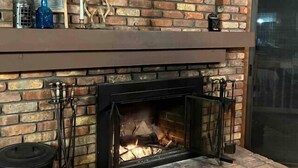A fireplace with a brick wall, a wooden mantel, and a wreath above it. - Gore Mountain Chalet - Moments From Adventure! (Ski, Hike, Explore) (North Creek)