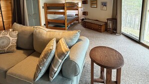 A cozy room with a sofa, a round wooden stool, a bunk bed, and a large window. - Gore Mountain Chalet - Moments From Adventure! (Ski, Hike, Explore) (North Creek)