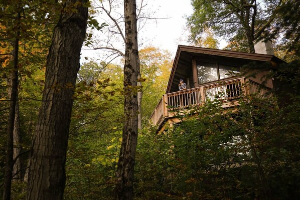 A wooden cabin with a balcony, surrounded by tall trees and dense foliage. - Gore Mountain Chalet - Moments From Adventure! (Ski, Hike, Explore) (North Creek)