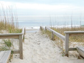 A wooden boardwalk leading to a beach with sand and seaweed.