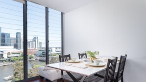 A dining area with a large window overlooking a cityscape and a river. - CityLights apartments (Melbourne)