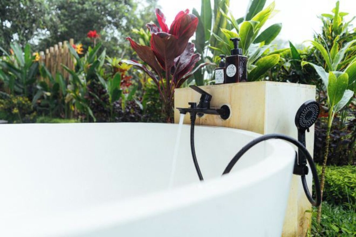 A white bathtub with a wooden structure, a black hose, and a shower head.