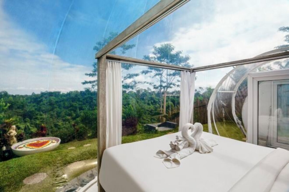 A room with a bed, a swan towel, and a view of a lush landscape.