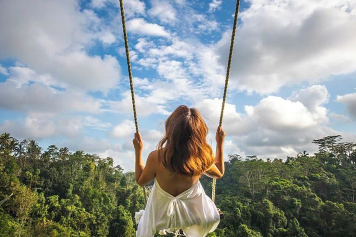A person on a swing with a natural landscape in the background.