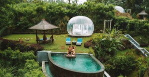 Ein privater Pool mit einem verglasten Whirlpool, umgeben von üppiger Vegetation und einer Holzterrasse.