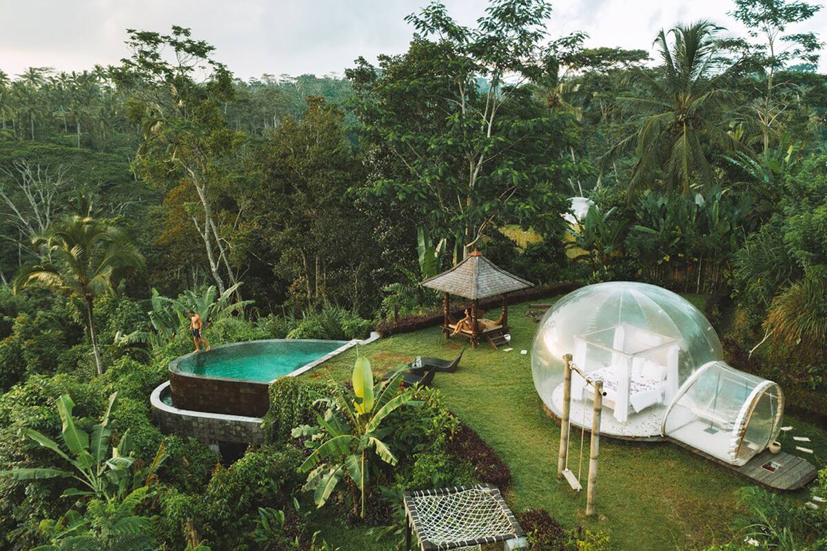 Une structure en forme de dôme transparent, située dans un jardin luxuriant, avec une piscine et un kiosque.