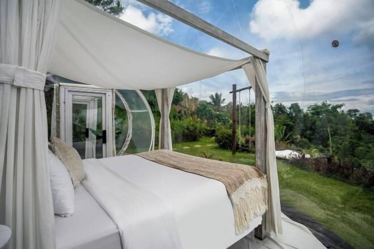 Une chambre à coucher avec un lit à baldaquin, une porte vitrée et une vue sur un jardin luxuriant.