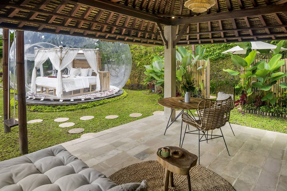 Un espace extérieur aménagé avec un coin salon abrité, comprenant un canapé confortable, une table en bois et une chaise en osier.