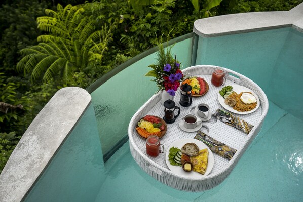 Un plateau de repas contenant divers aliments et boissons, posé sur un balcon donnant sur une végétation luxuriante.