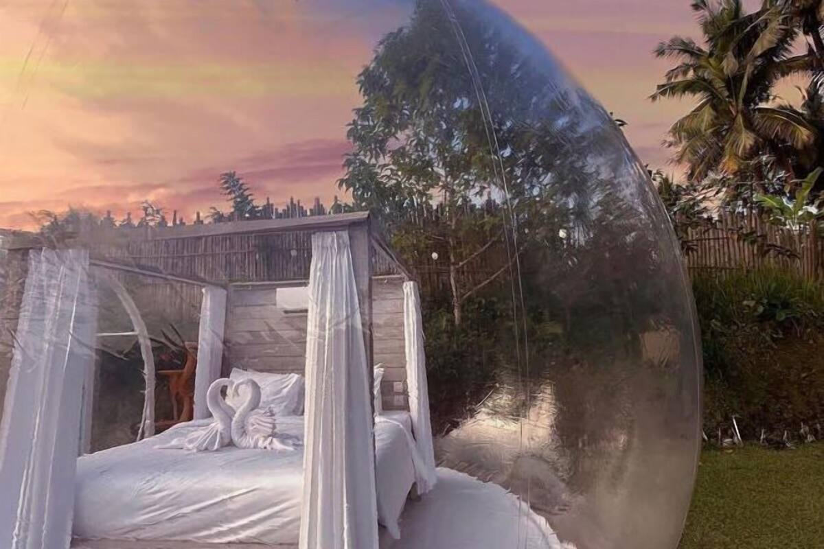 Un lit à baldaquin, entouré d’une clôture, avec des palmiers en arrière-plan.