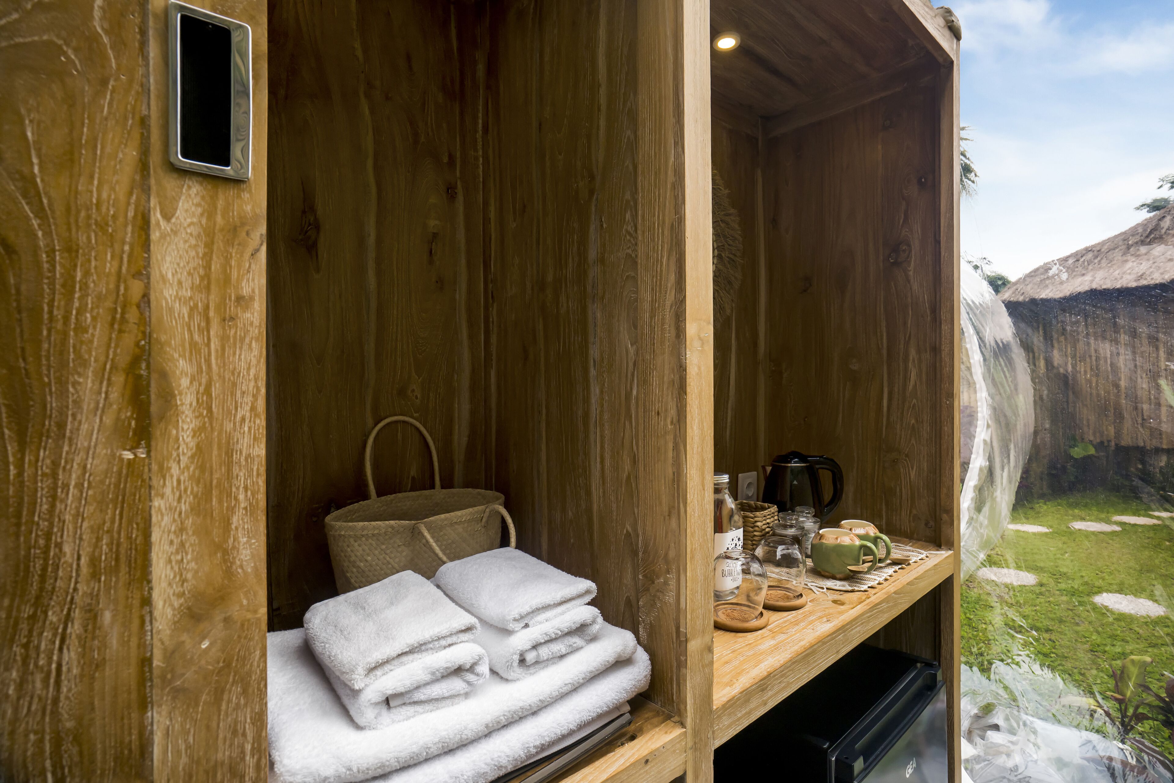 A wooden cabin with a wooden shelf holding towels, a woven bag, and a coffee maker.