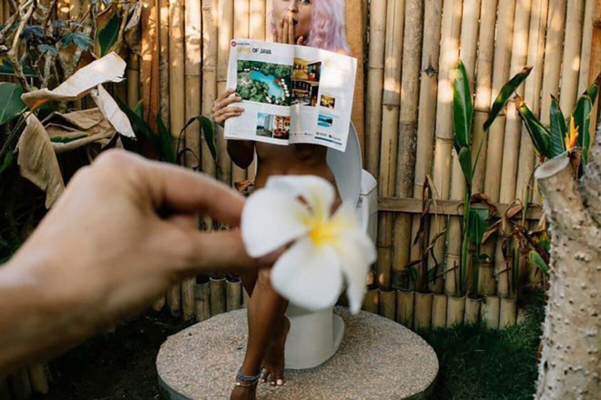 Une personne tient un magazine présentant des photos de piscines et de complexes hôteliers, et se tient devant une clôture en bambou.