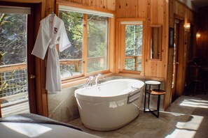A bathroom with a freestanding bathtub, a towel rack, and a window with a view of trees.