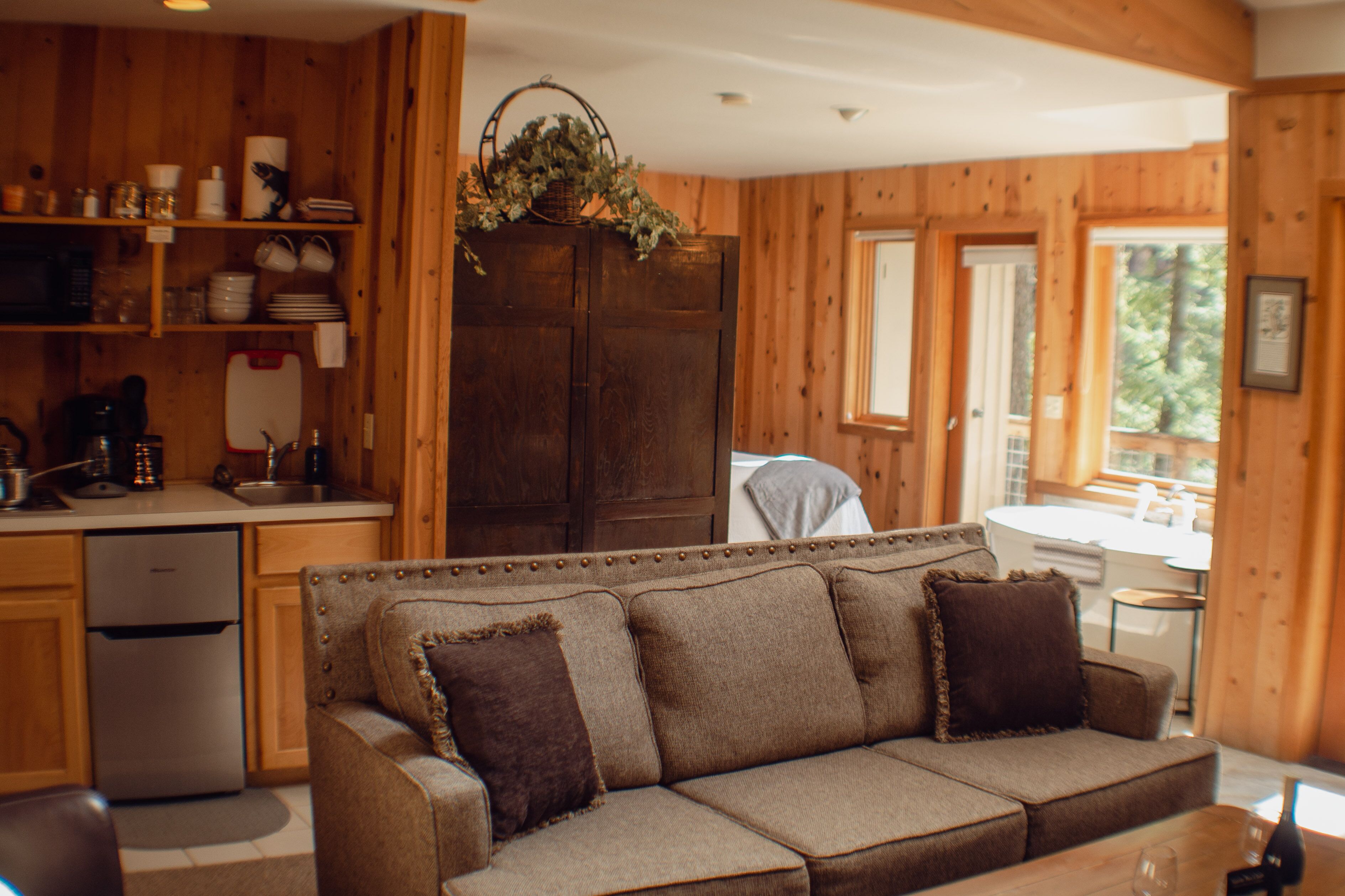 A cozy cabin interior with a wooden interior, a sofa with cushions, a kitchen area with shelves, and a dining table.