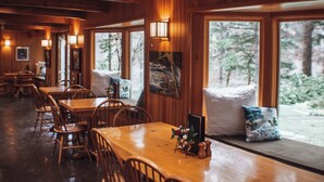 A cozy restaurant with wooden interiors, large windows, and a dining area with tables and chairs.