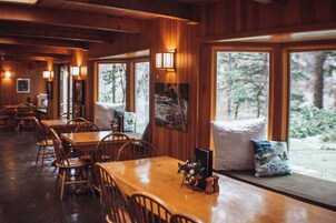 Un restaurante acogedor con interiores de madera, ventanas amplias y un comedor con mesas y sillas.