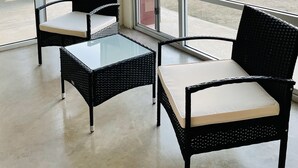 Un balcon agrémenté de deux fauteuils en osier et d’une table en verre, donnant sur un espace paysager avec des plantes et offrant une vue lointaine sur des collines.