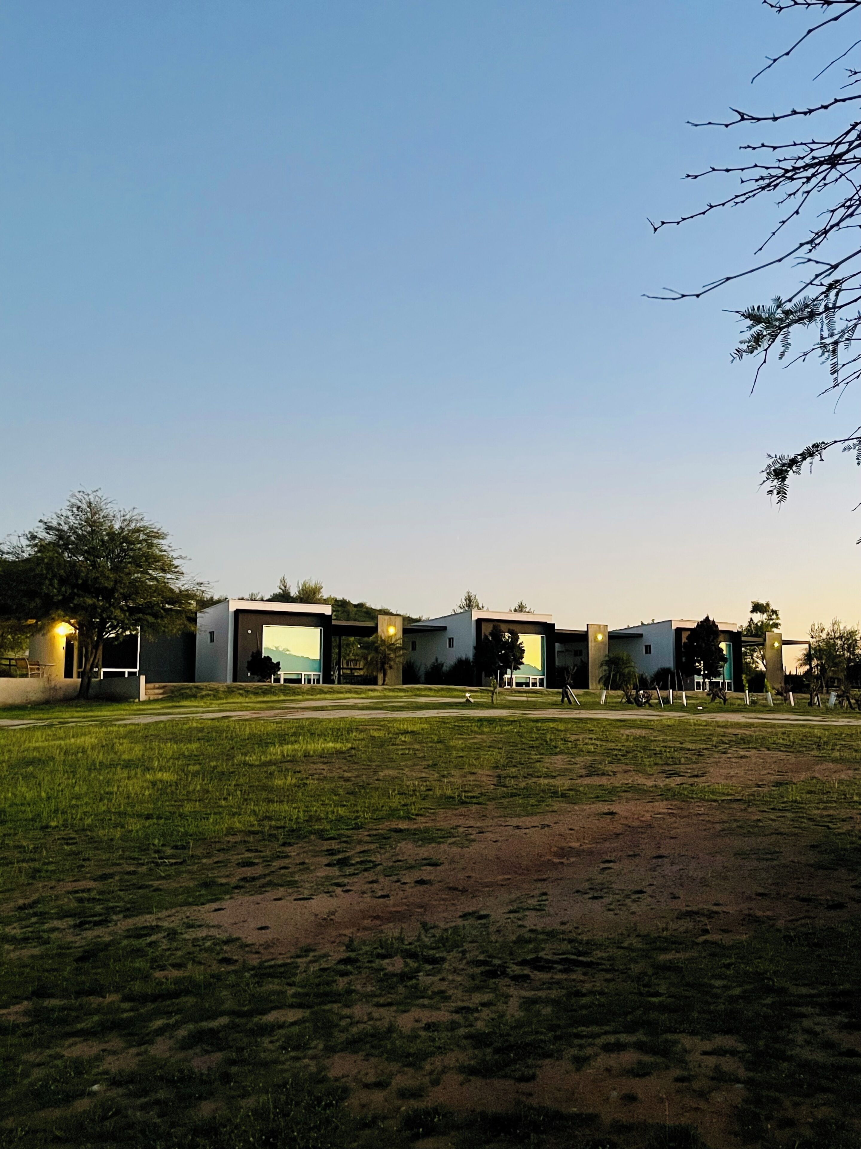 A modern building complex with multiple structures, a grassy field, and a clear sky.
