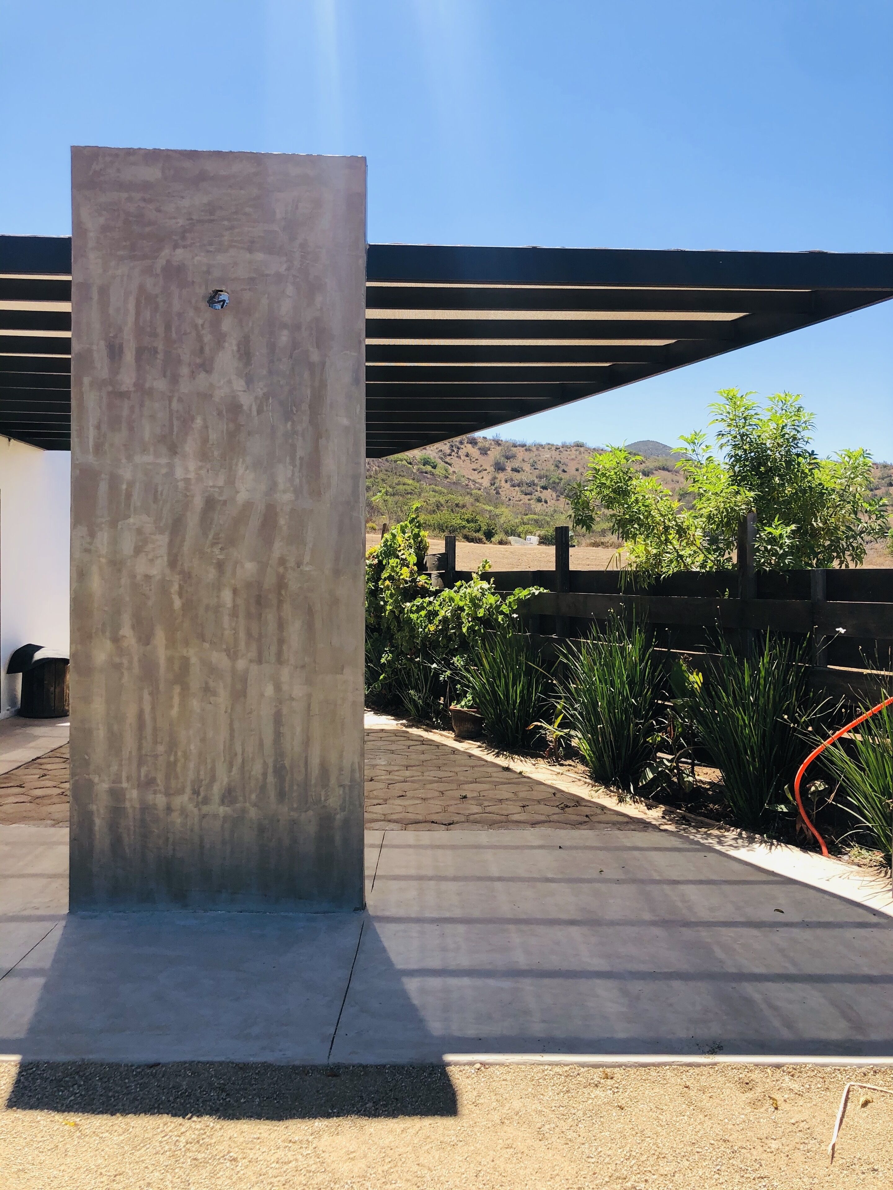 A concrete pillar in an outdoor area with a paved walkway, surrounded by greenery and a view of hills in the background.