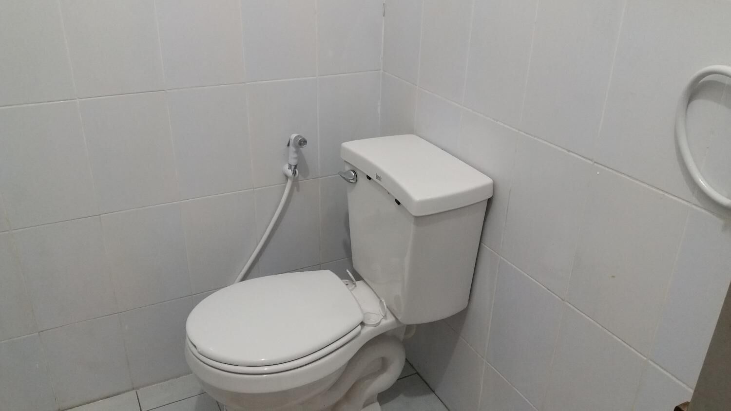 Des toilettes blanches, avec une cuvette et un siège-bidet, dans une salle de bain dont les murs sont recouverts de carreaux blancs.