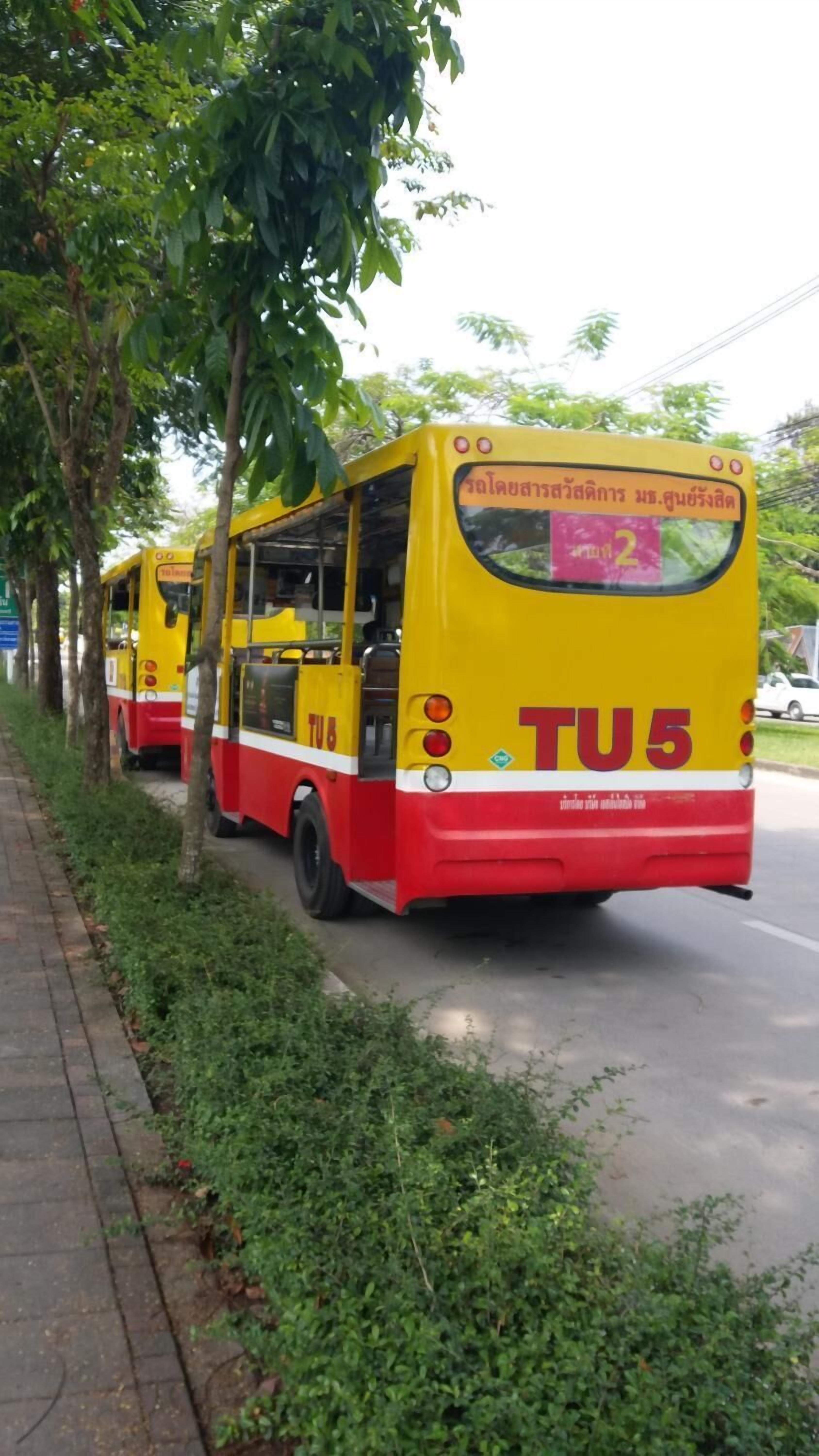 A yellow and red bus with the number TU5 parked on a road lined with trees.