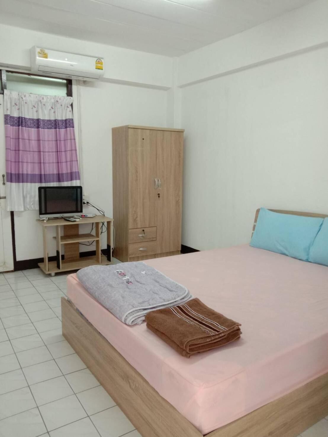A bedroom with a bed, a wardrobe, a desk with a computer, and an air conditioner.