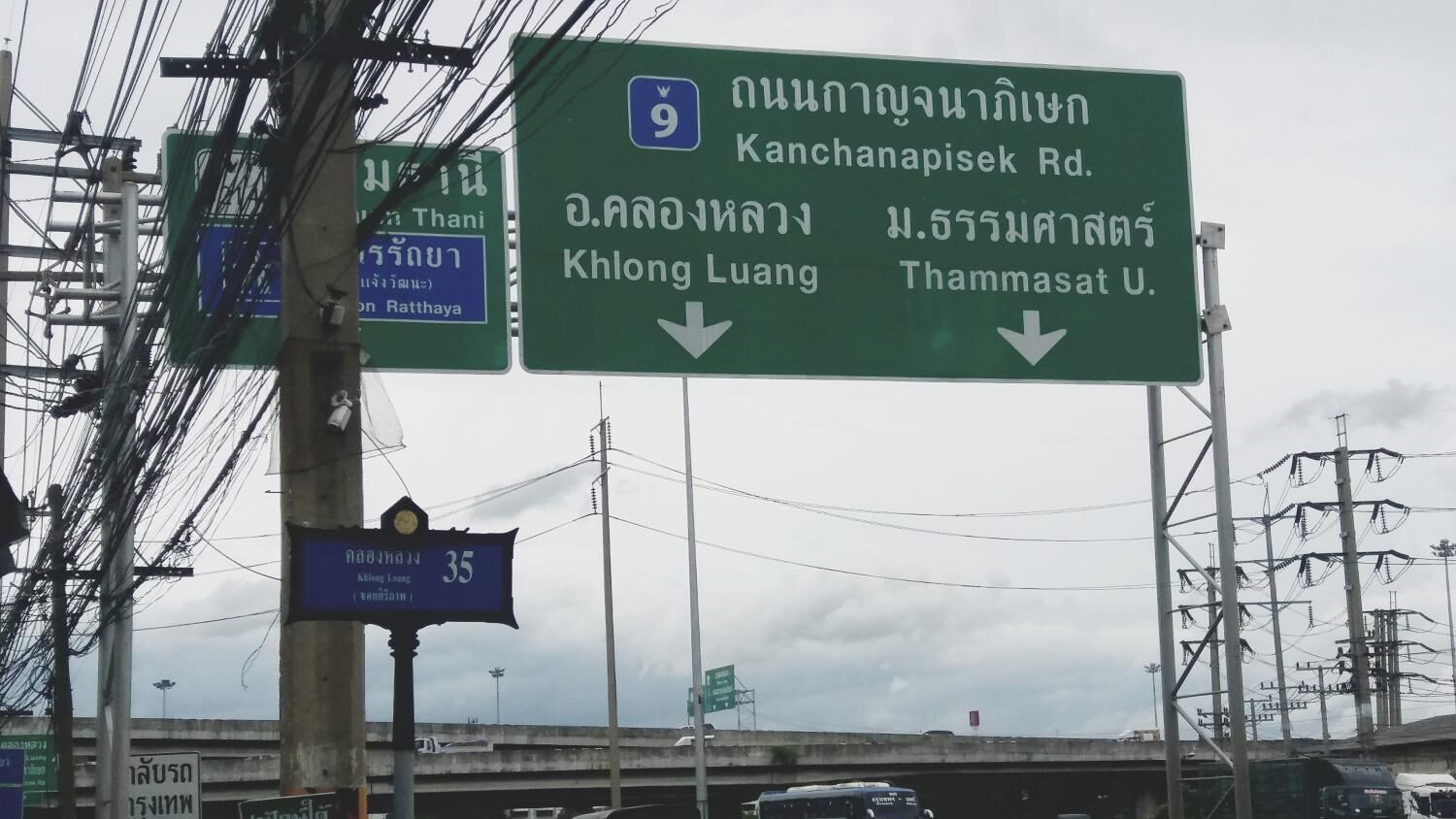 A green highway sign with white text indicating directions to Kanchanapisek Rd., Khlong Luang, and Thammasat U.