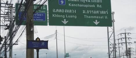 A green highway sign with white text indicating directions to Kanchanapisek Rd., Khlong Luang, and Thammasat U.