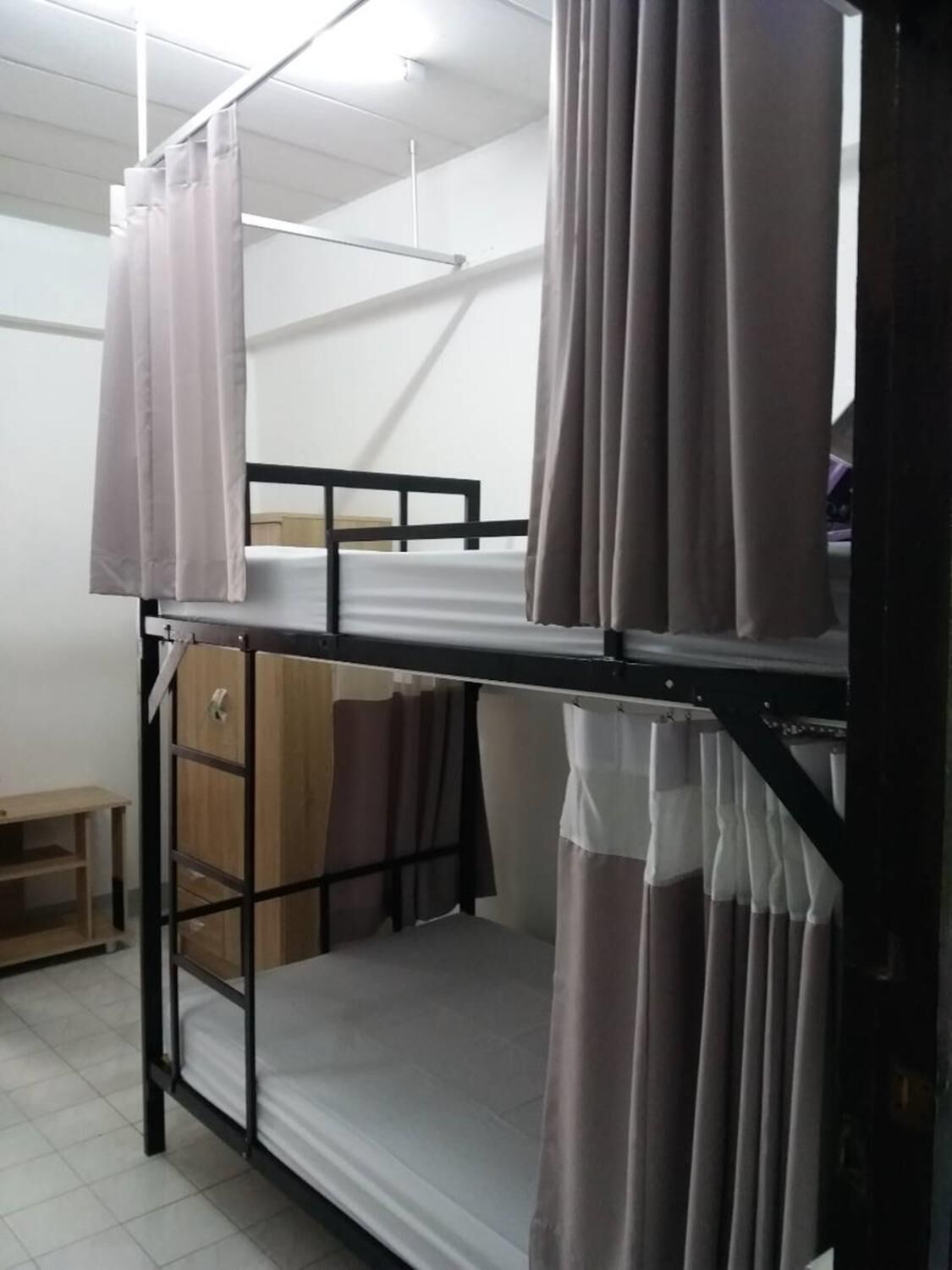 A bunk bed with curtains, a wooden wardrobe, and a small table in a dormitory room.
