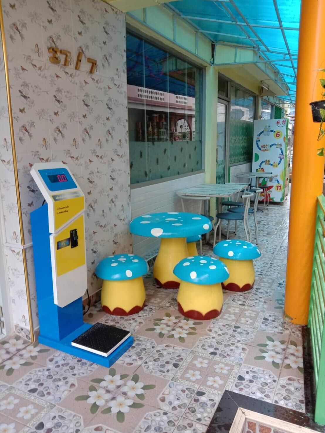 A children's play area with a digital weighing scale, a vending machine, and mushroom-shaped stools.