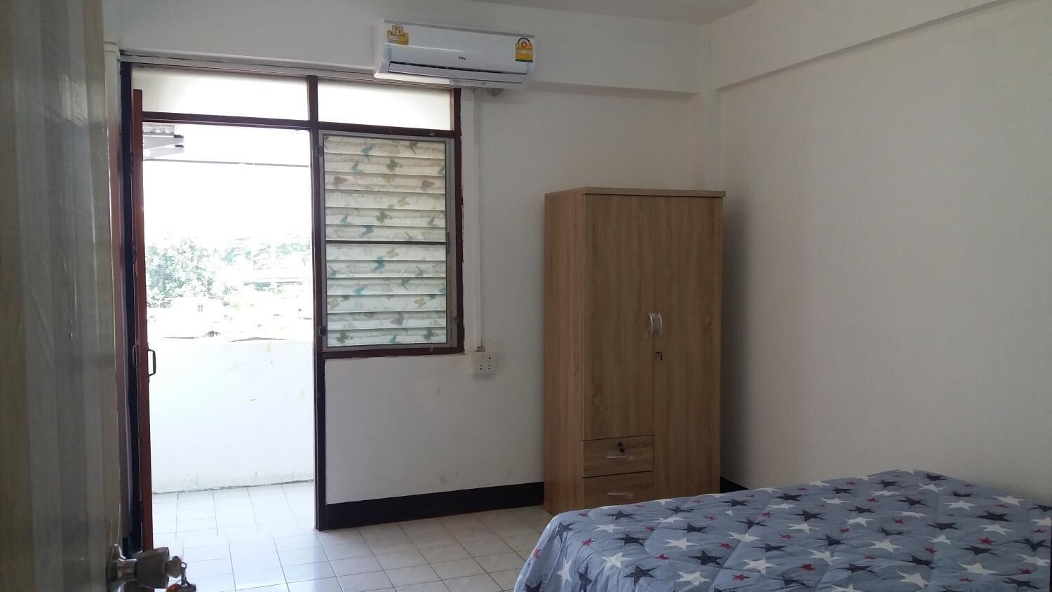 A bedroom with a bed, a wardrobe, a window with blinds, and an air conditioning unit.
