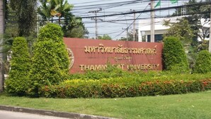 Señal de la Universidad Thammasat rodeada de follaje cuidado y un cielo despejado.